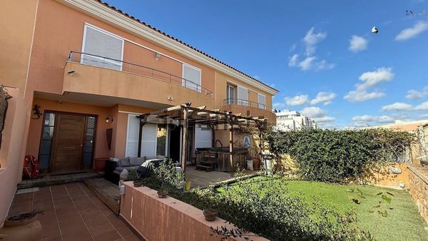 Patio y jardín junto a una casa de dos plantas color melocotón bajo un cielo azul.