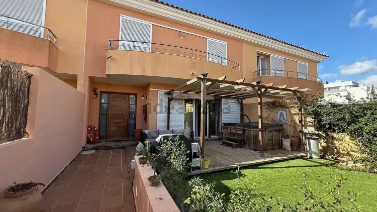 Casa de color melocotón bañada por el sol, con patio, pérgola y césped verde bajo un cielo azul.