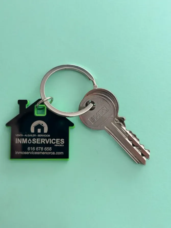 Llavero de INM Services con forma de casa y llaves plateadas sobre fondo verde menta.