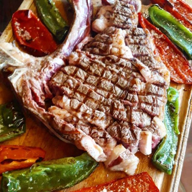 Un filete grande está rodeado de pimientos y tomates sobre una tabla de cortar de madera.