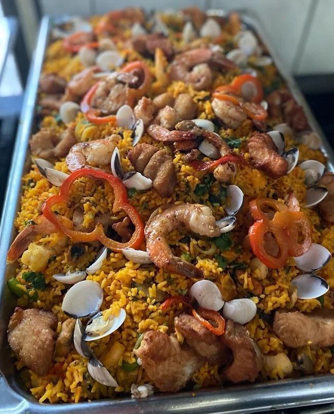 Una sartén llena de arroz, camarones, almejas, pimientos y otras verduras.