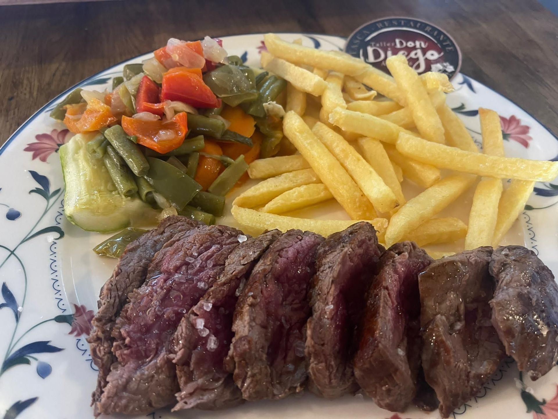 Un plato de comida con carne, patatas fritas y verduras en una mesa.