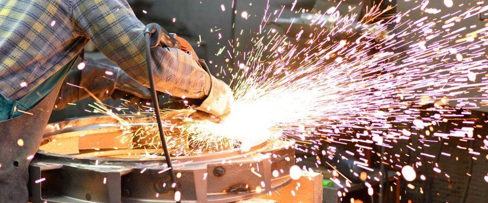 Ein Arbeiter benutzt einen Winkelschleifer und erzeugt helle Funken auf einer Metalloberfläche.