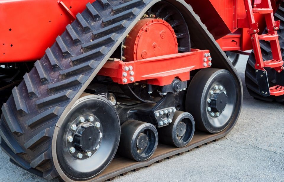Rotes Kettenfahrzeug für die Landwirtschaft mit großen schwarzen Ketten und Rädern auf einer Betonfläche