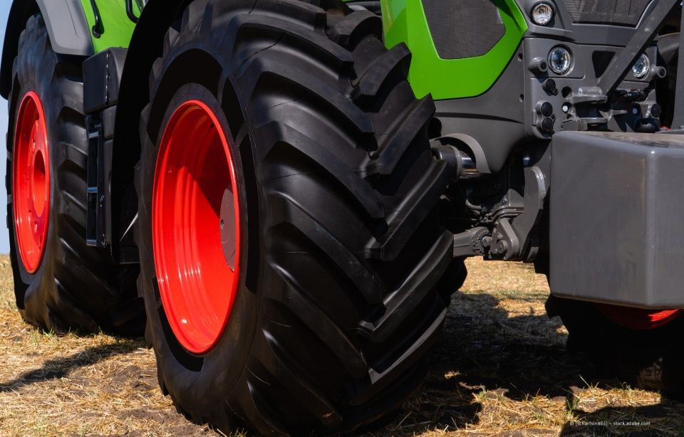 Nahaufnahme der großen schwarzen Reifen eines grünen Traktors mit leuchtend roten Felgen auf trockenem Boden.
