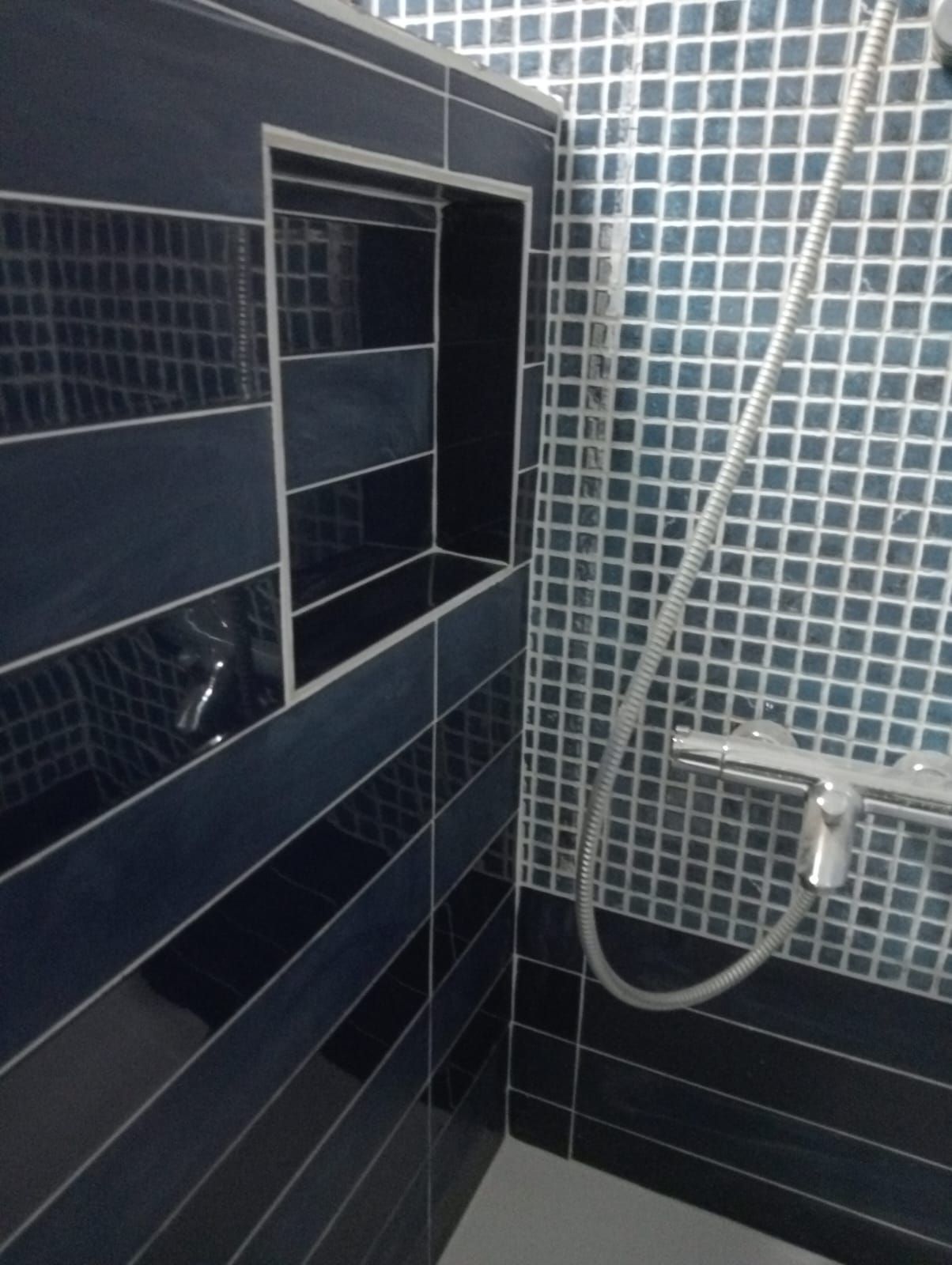 Un baño con azulejos azules y un cabezal de ducha.