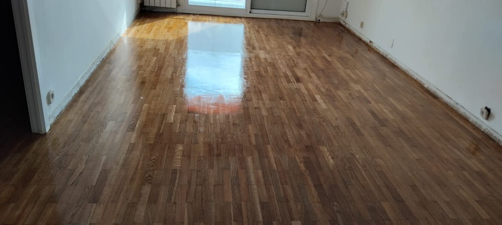 Una sala de estar con suelo de madera y paredes blancas.
