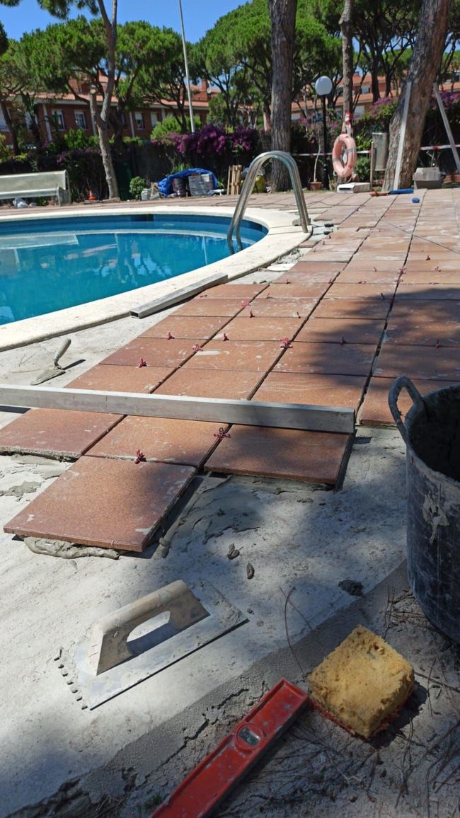 Se está construyendo una pasarela de baldosas alrededor de una piscina.