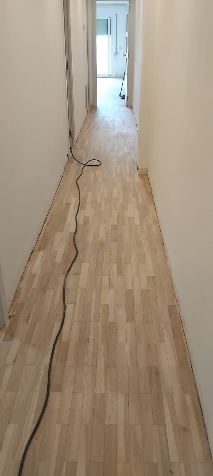 Un pasillo largo con suelo de madera y un cordón negro.