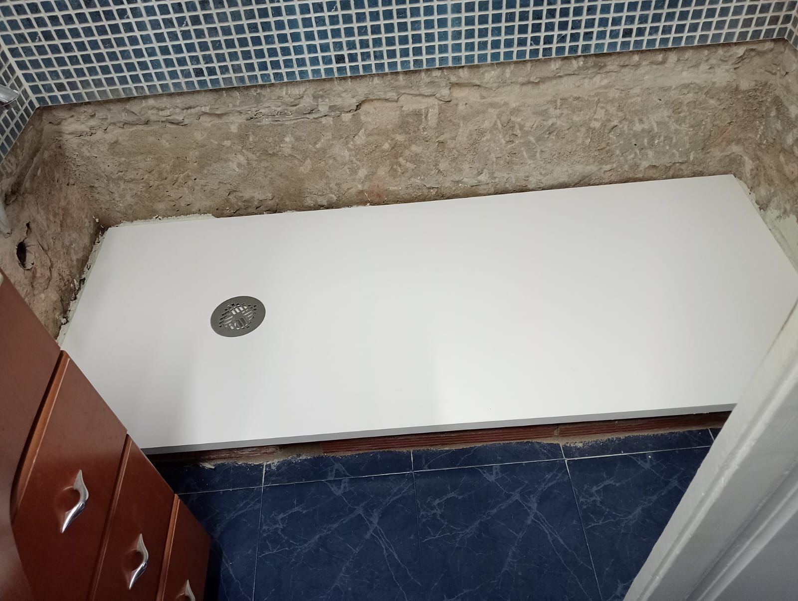 Un baño con plato de ducha blanco y desagüe.