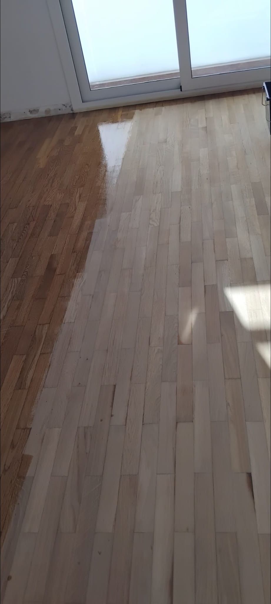 Se está pintando un piso de madera en una habitación con ventana.