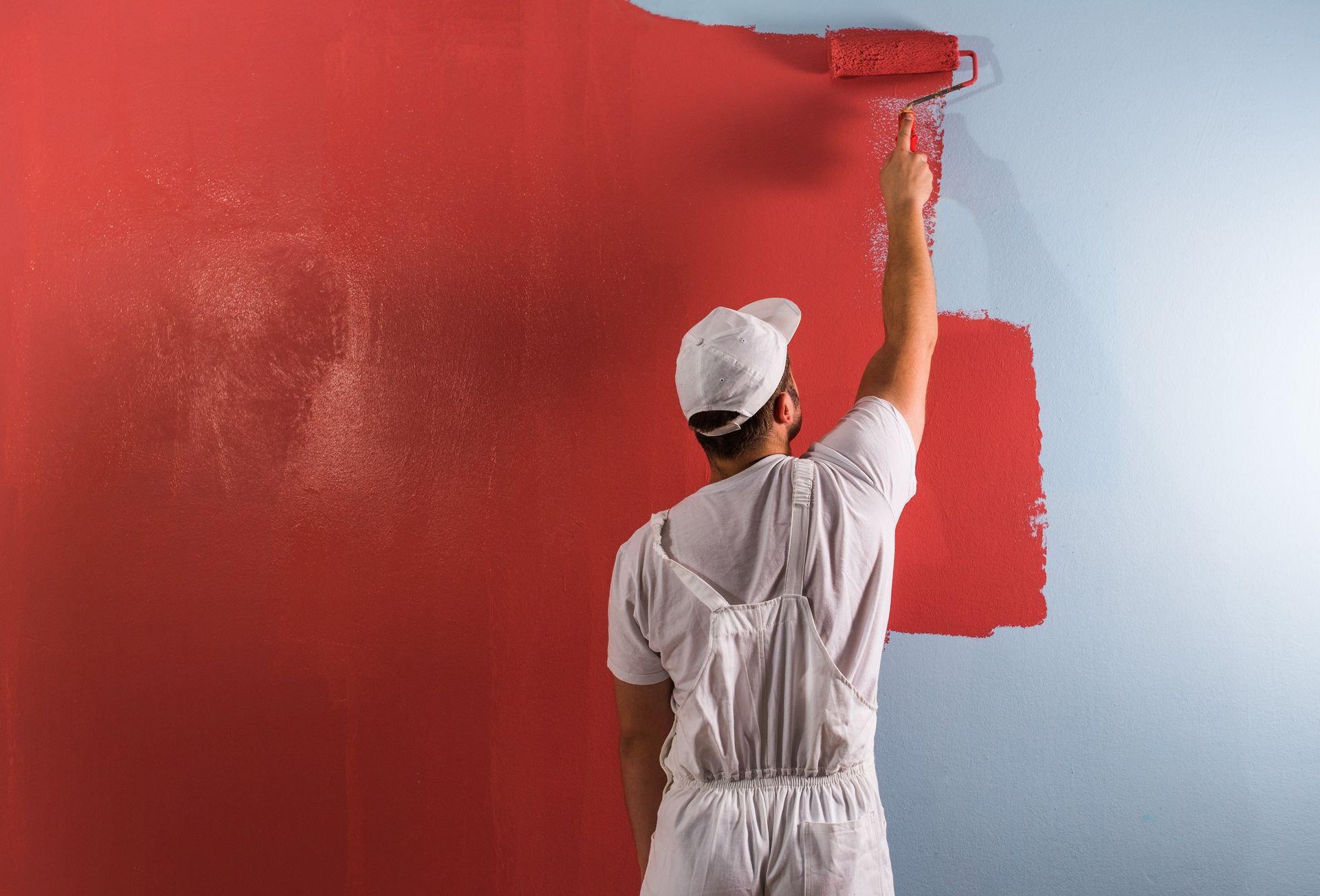 Un hombre está pintando una pared de rojo con un rodillo.