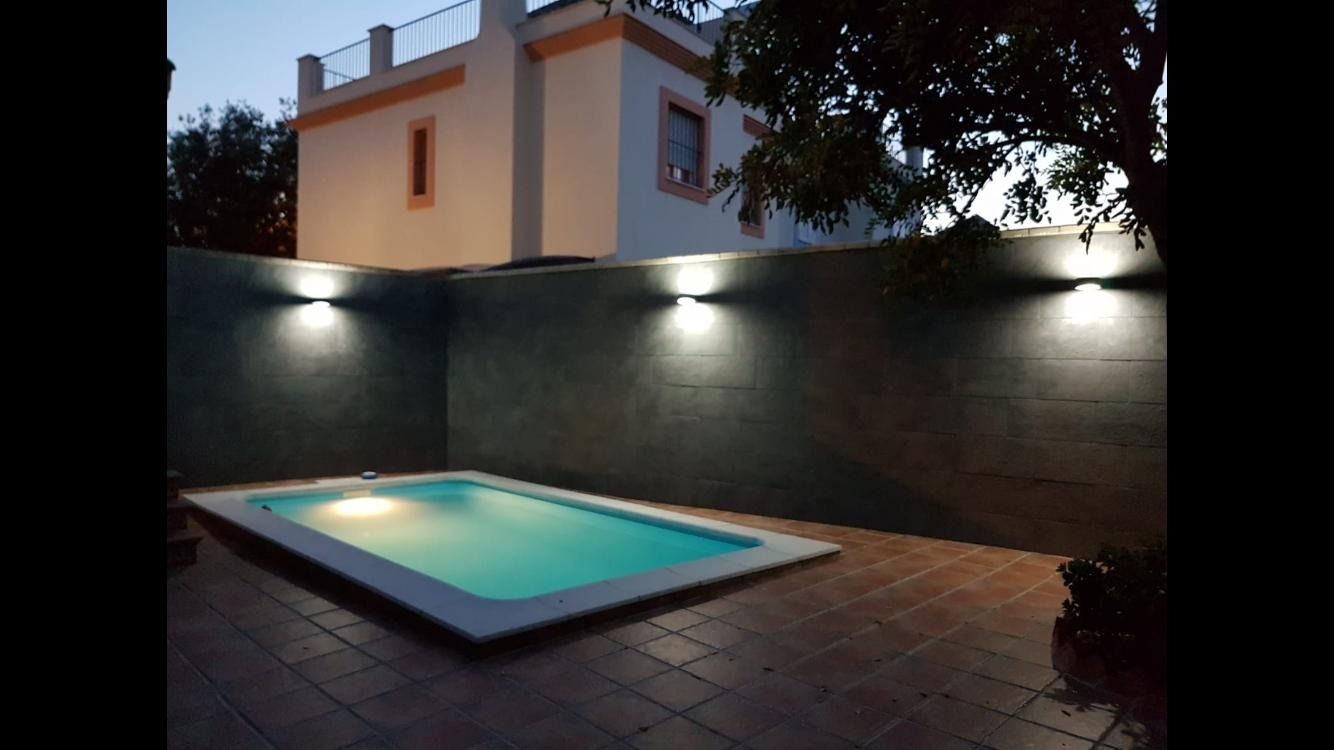 Una piscina está iluminada en el patio trasero de una casa.