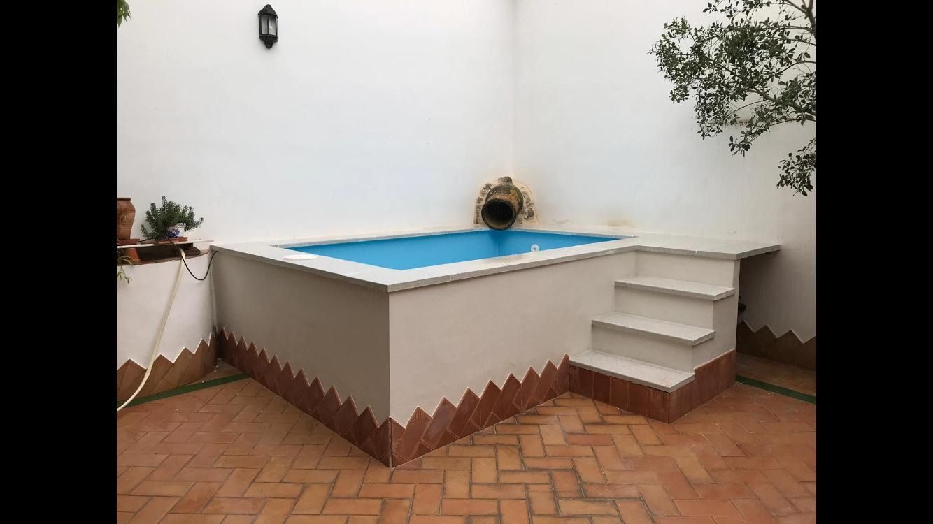 Una pequeña piscina con escaleras y un árbol al fondo.