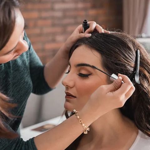 Una mujer está aplicando rímel en las cejas de otra mujer.