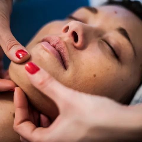 Una mujer con uñas rojas está recibiendo un masaje en la cara.