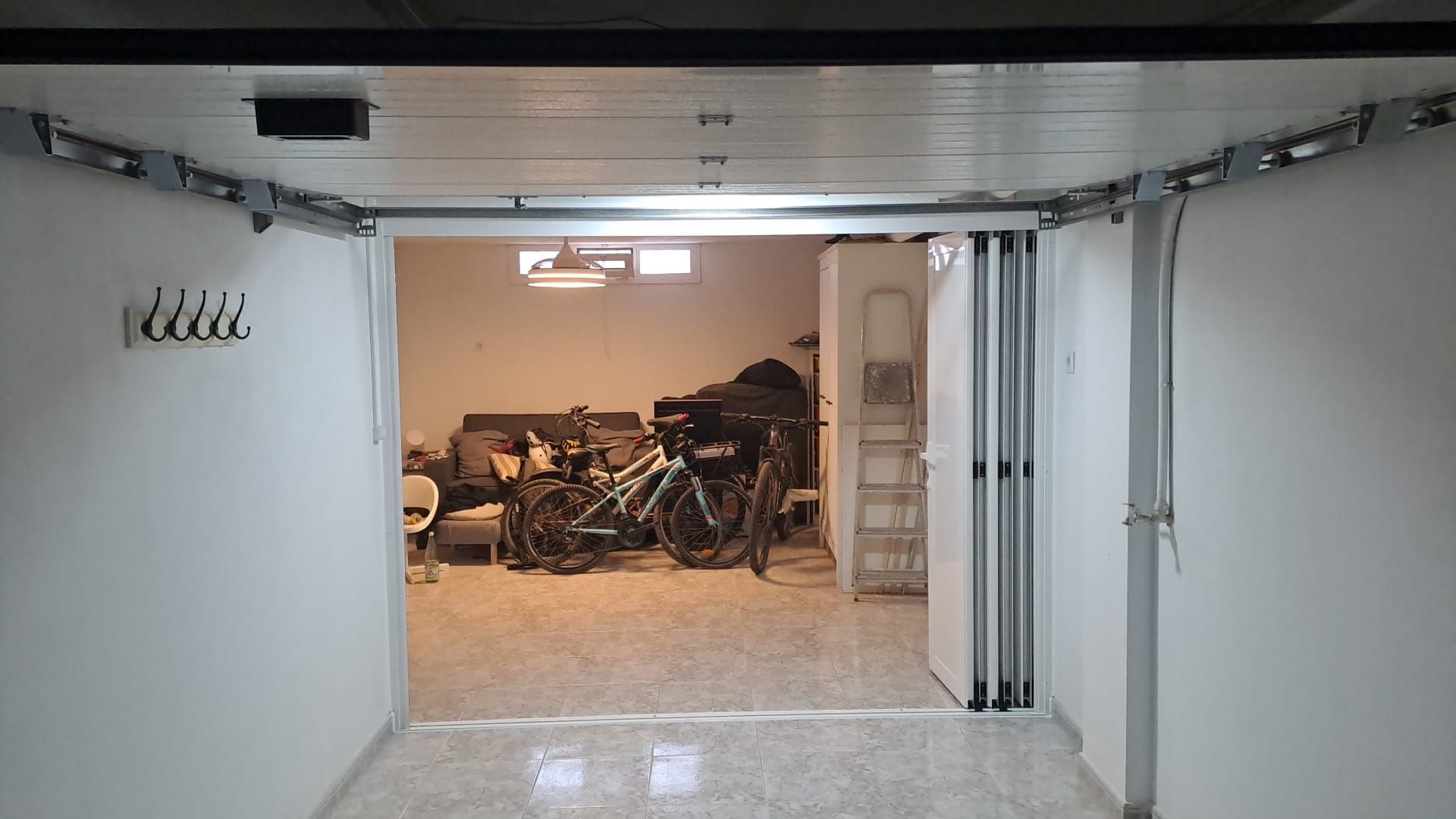 Dos bicicletas están aparcadas en un garaje con una sala de estar al fondo.
