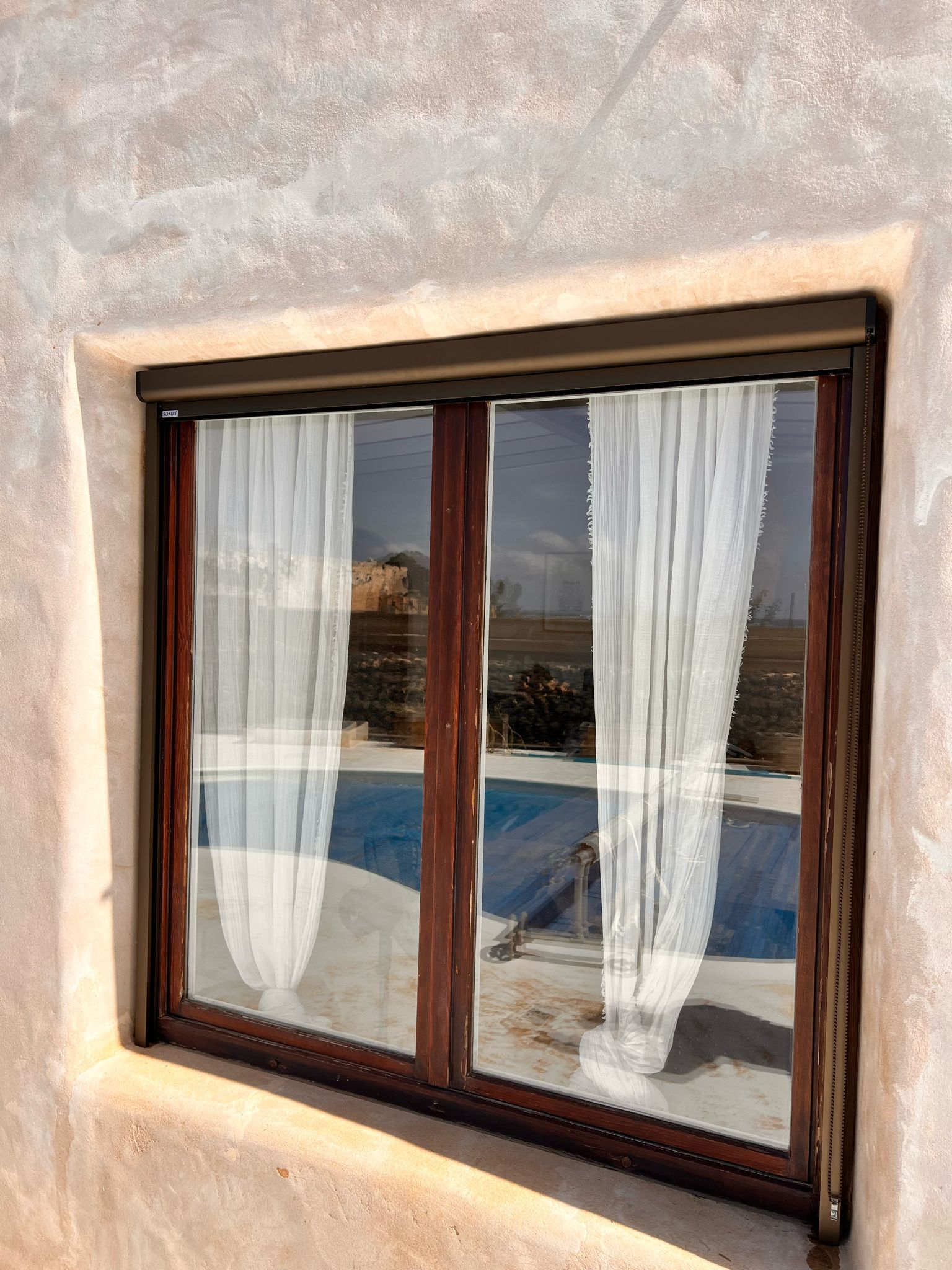 Una ventana con cortinas blancas y vista a una piscina.