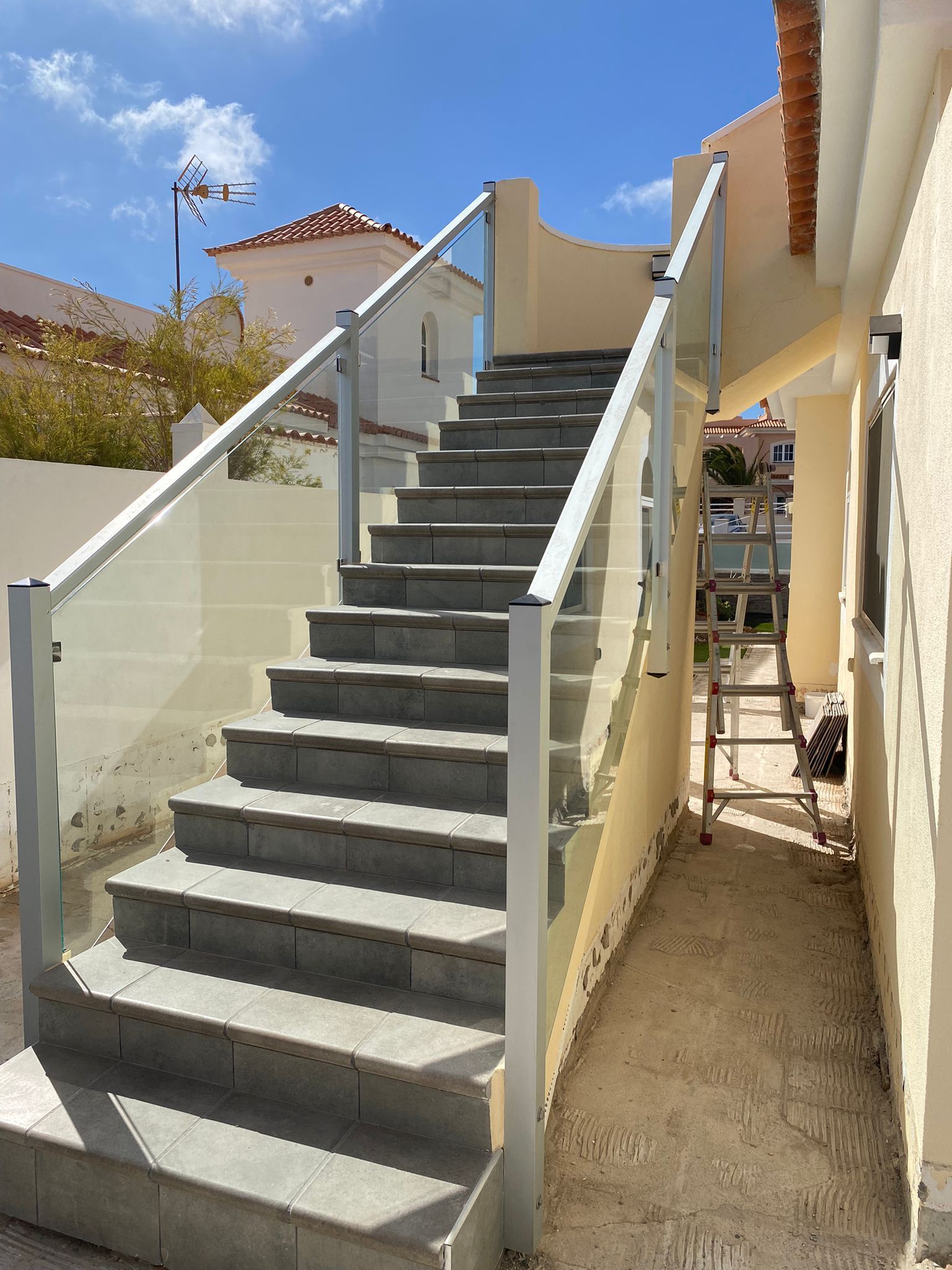 Un conjunto de escaleras con barandilla de cristal y una escalera al fondo.