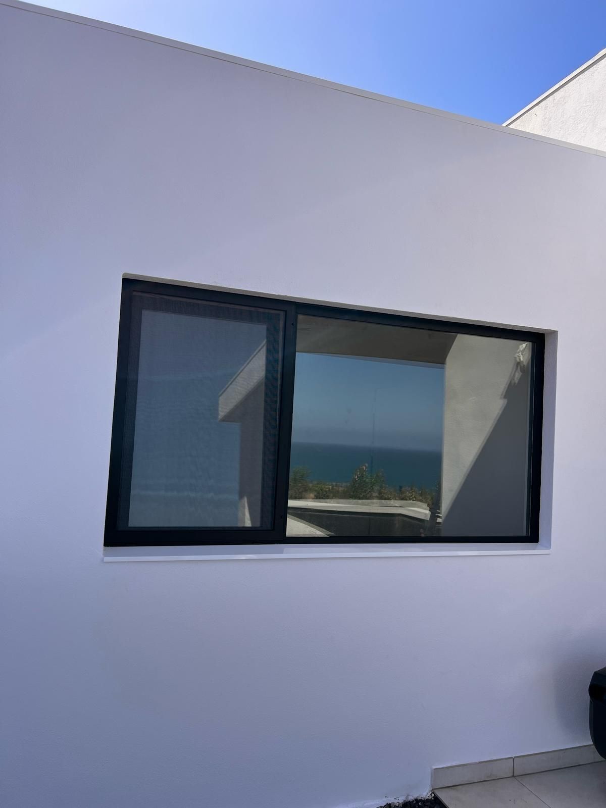 Una gran ventana en una pared blanca con vista al océano.