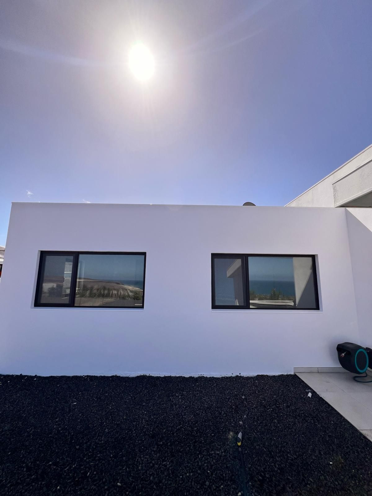 Un edificio blanco con dos ventanas y un cielo azul al fondo.