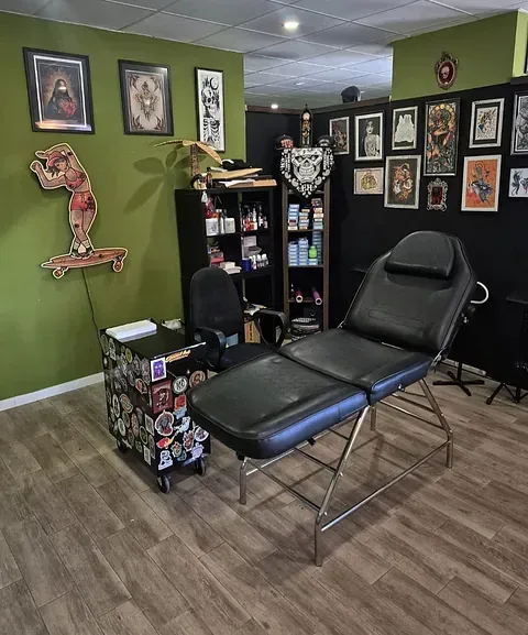 Un puesto de tatuaje con una camilla negra ajustable, un carrito con ruedas cubierto de pegatinas.