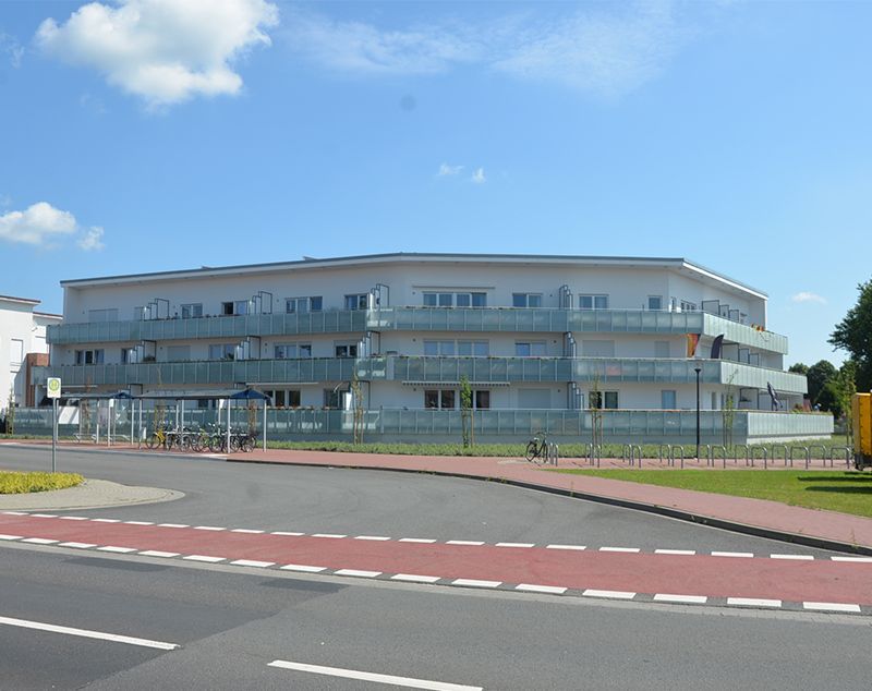 Ein großes weißes Gebäude mit Balkonen liegt neben einer Straße