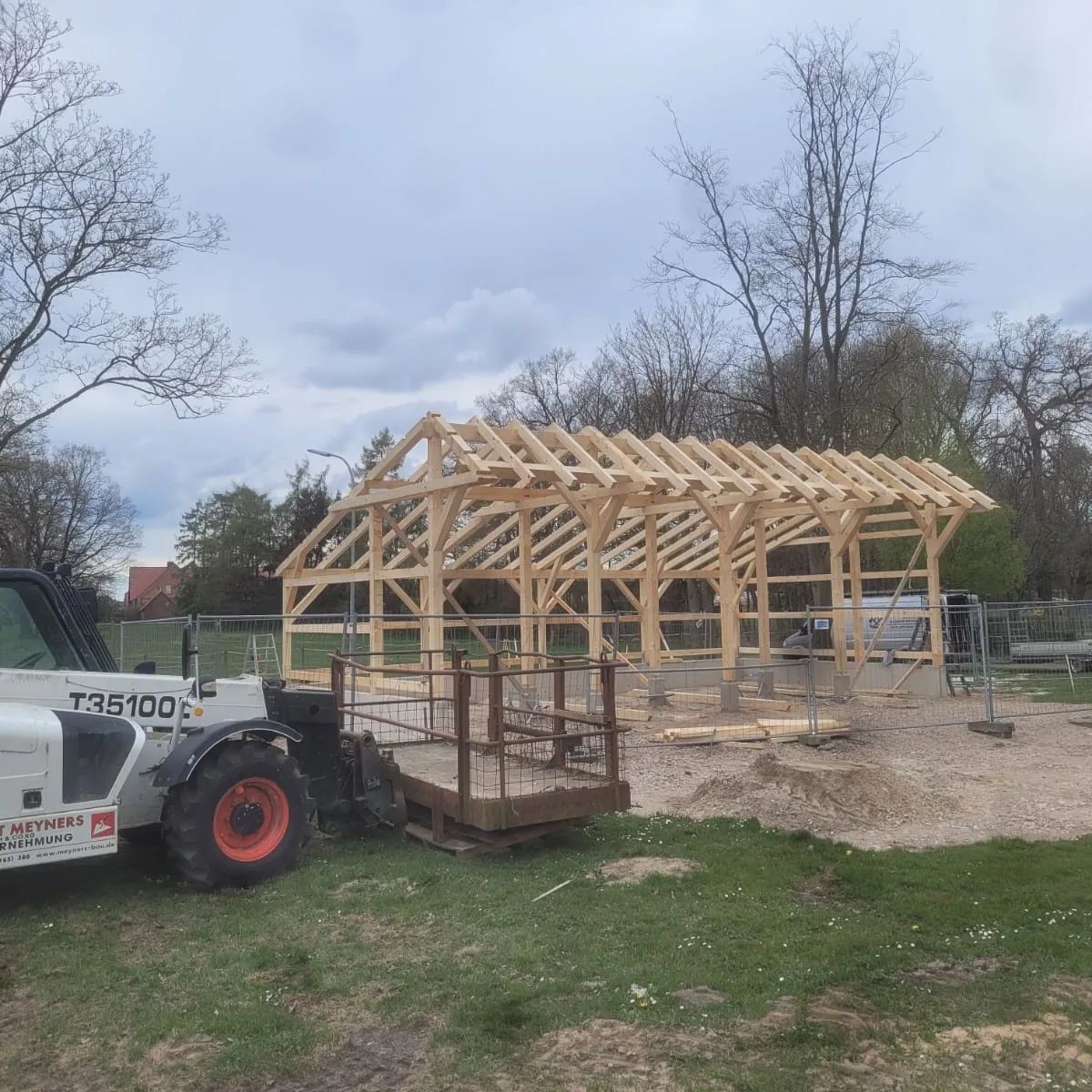 Ein Traktor steht vor einer im Bau befindlichen Holzkonstruktion.