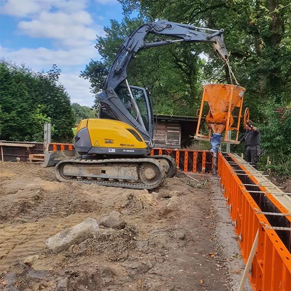 Ein gelber Bagger gießt Beton in einen orangefarbenen Eimer