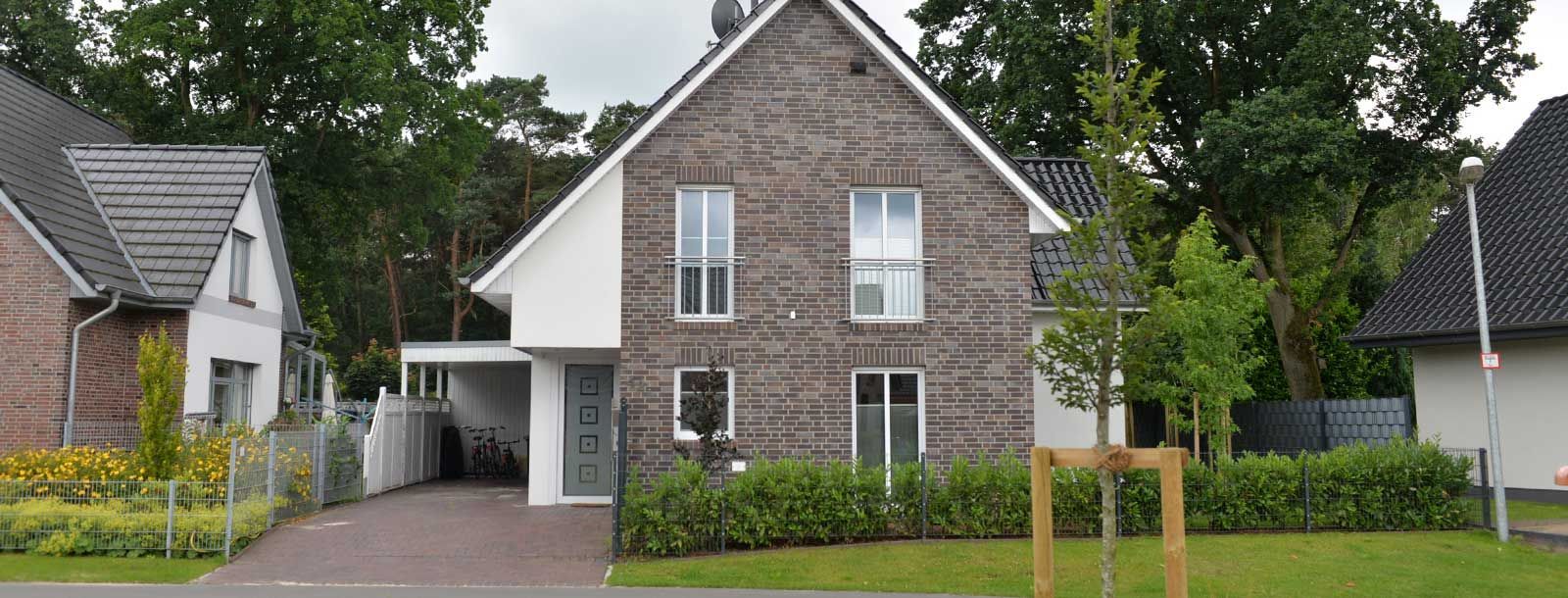 Ein Backsteinhaus mit weißen Verzierungen ist von Bäumen und Büschen umgeben.