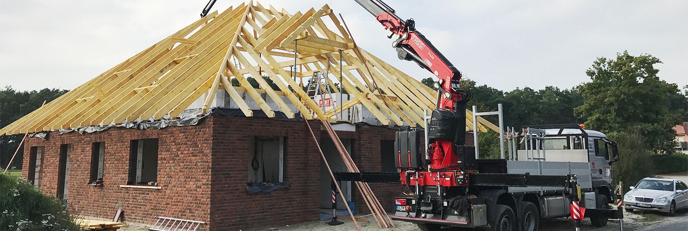 Ein Kran hebt eine Holzkonstruktion auf ein Backsteingebäude.