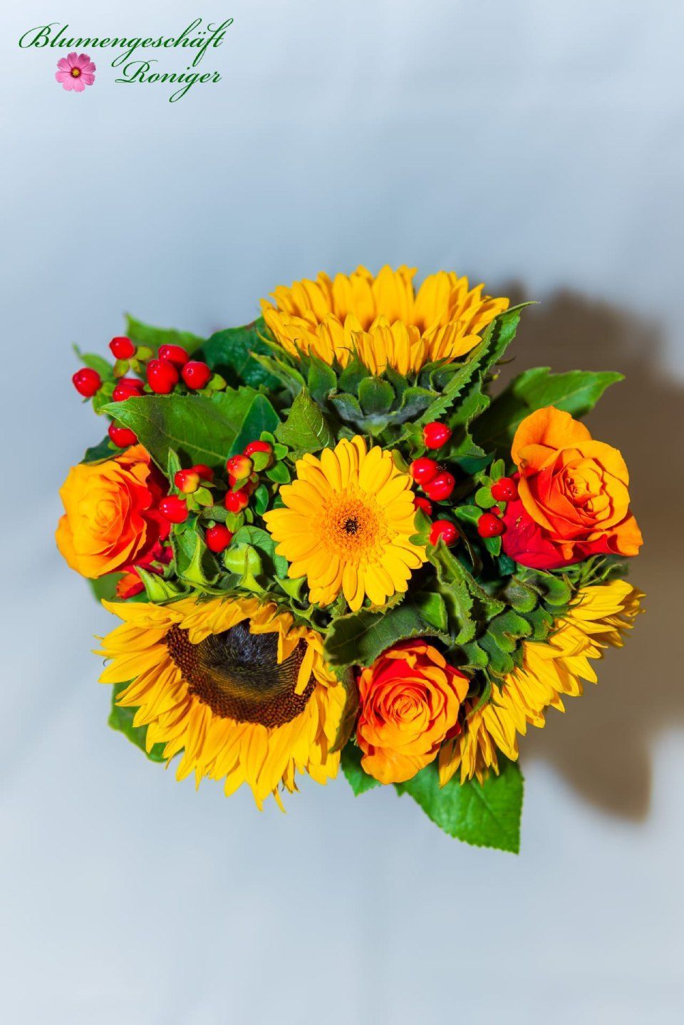 Ein Strauß gelber Blumen mit roten Beeren und grünen Blättern