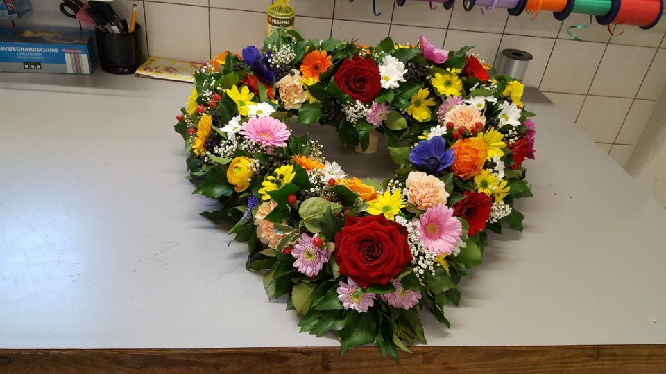 Auf einem Tisch steht ein herzförmiger Blumenkranz.