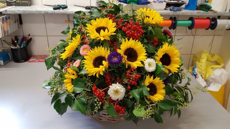 Auf einem Tisch steht ein Korb voller Sonnenblumen und anderer Blumen.
