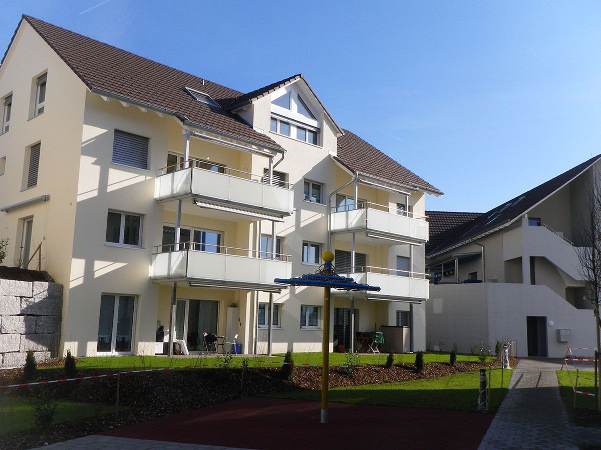 Mehrfamilienhaus mit Balkonen und einem kleinen Spielplatz an einem sonnigen Tag.
