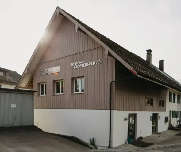 Braun-weißes Gebäude mit schrägem Dach, Fenstern und Firmenschild im Freien.