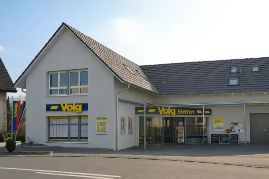 Außenansicht eines Volg-Supermarkts mit gelber und blauer Beschilderung; graues Gebäude mit schrägem Dach.
