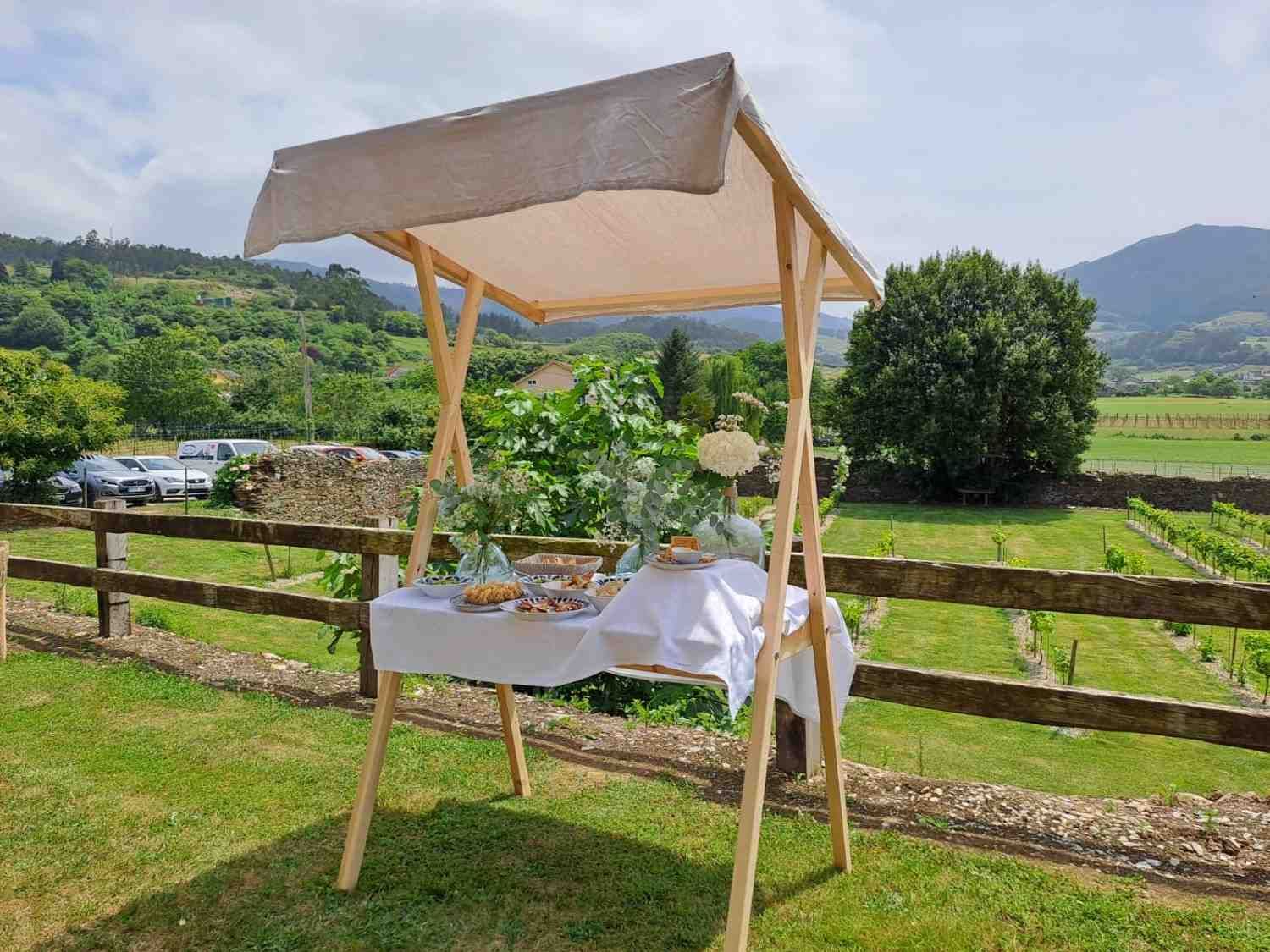 Un puesto de mercado de madera con un mantel blanco y golosinas, situado al aire libre con un fondo de montañas.