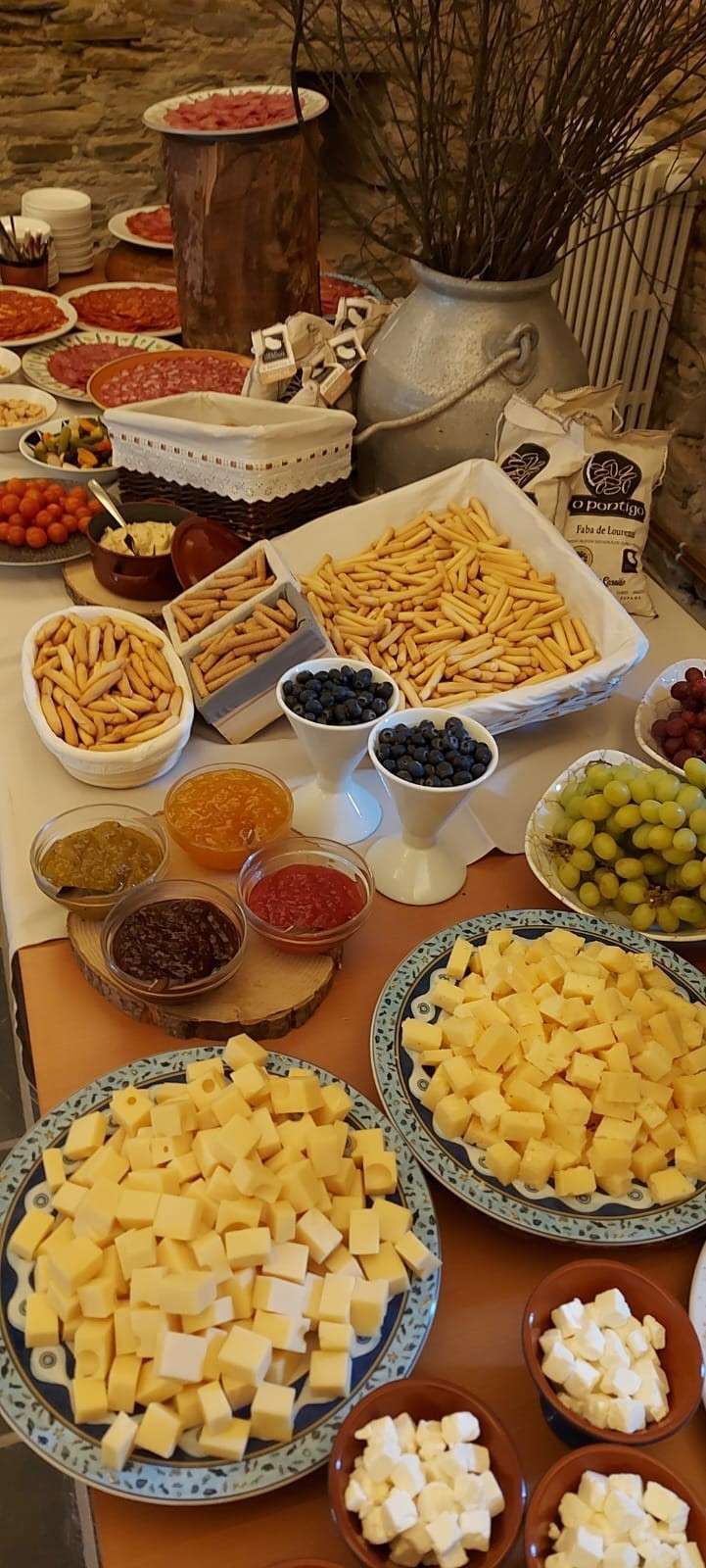 Una mesa de buffet muestra diversos alimentos: quesos, pastas, frutas y pequeños cuencos con aderezos.