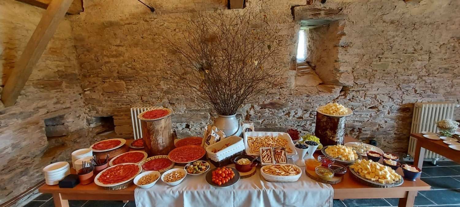 Mesa de buffet en una sala de piedra con diversos platos de comida, incluidos tomates, queso y palomitas de maíz.