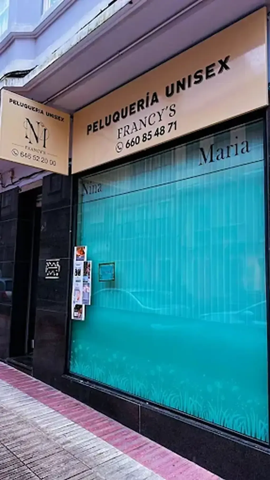 Exterior de una peluquería unisex, "Francy's", con una ventana tintada en verde azulado y un cartel.