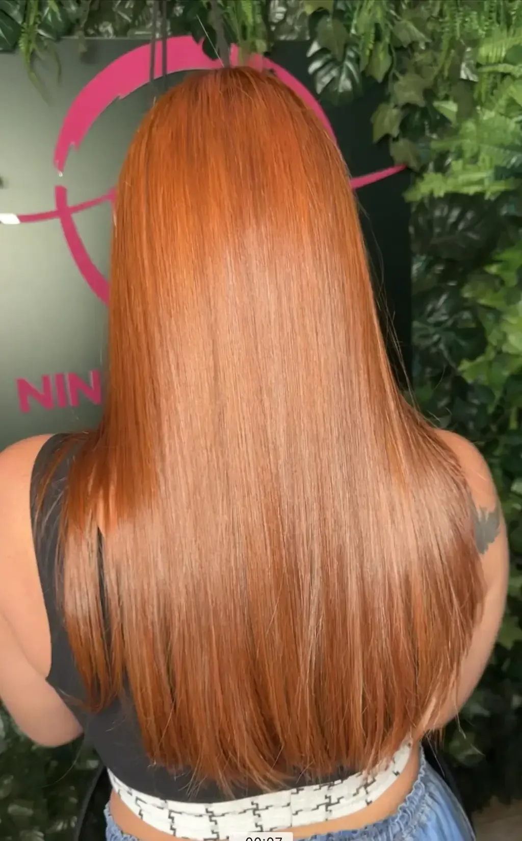 Mujer con cabello largo, liso y rojizo anaranjado. Vista trasera en un salón de belleza.