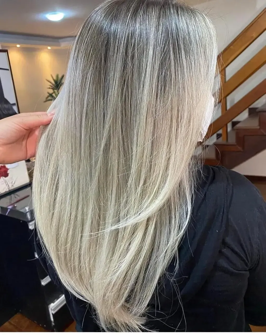 Mujer con cabello largo, rubio y con reflejos grises. En el interior, alguien le toca el pelo.