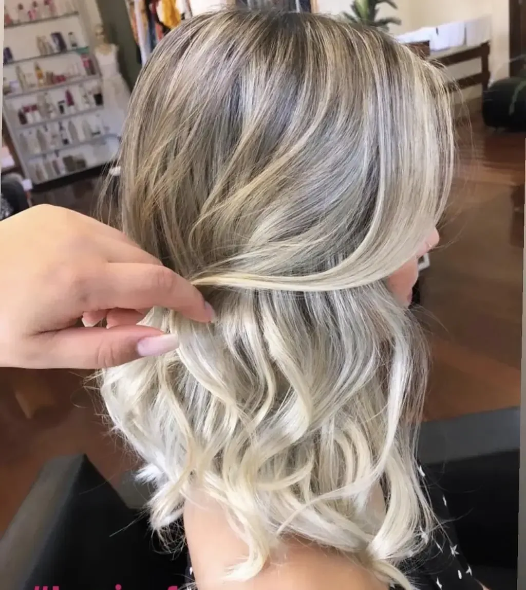 Cabello rubio peinado en ondas sueltas, peinado por una mano con uñas cuidadas en un salón de belleza.