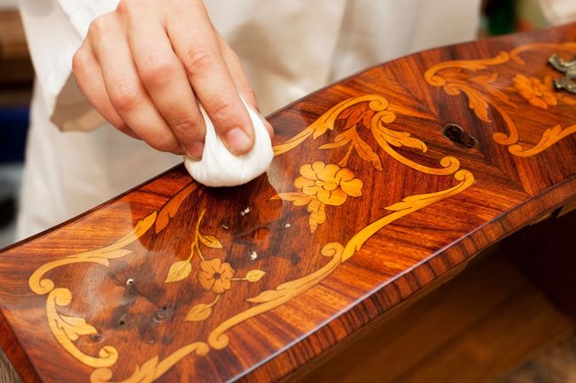 Polissage à la main d’une surface en bois brillante ornée de motifs floraux, à l’aide d’un chiffon