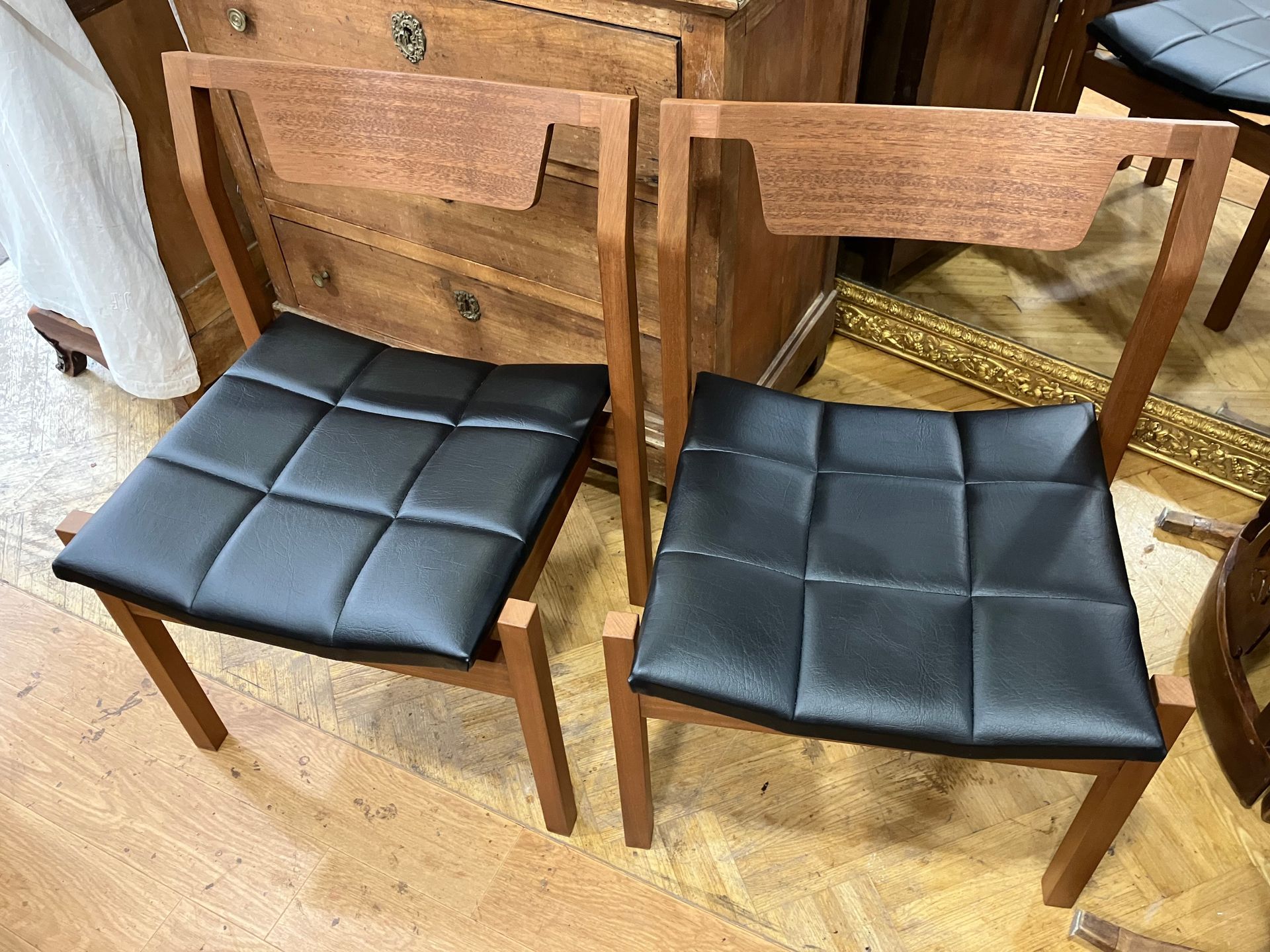 Deux chaises en bois avec des assises rembourrées noires devant un meuble en bois