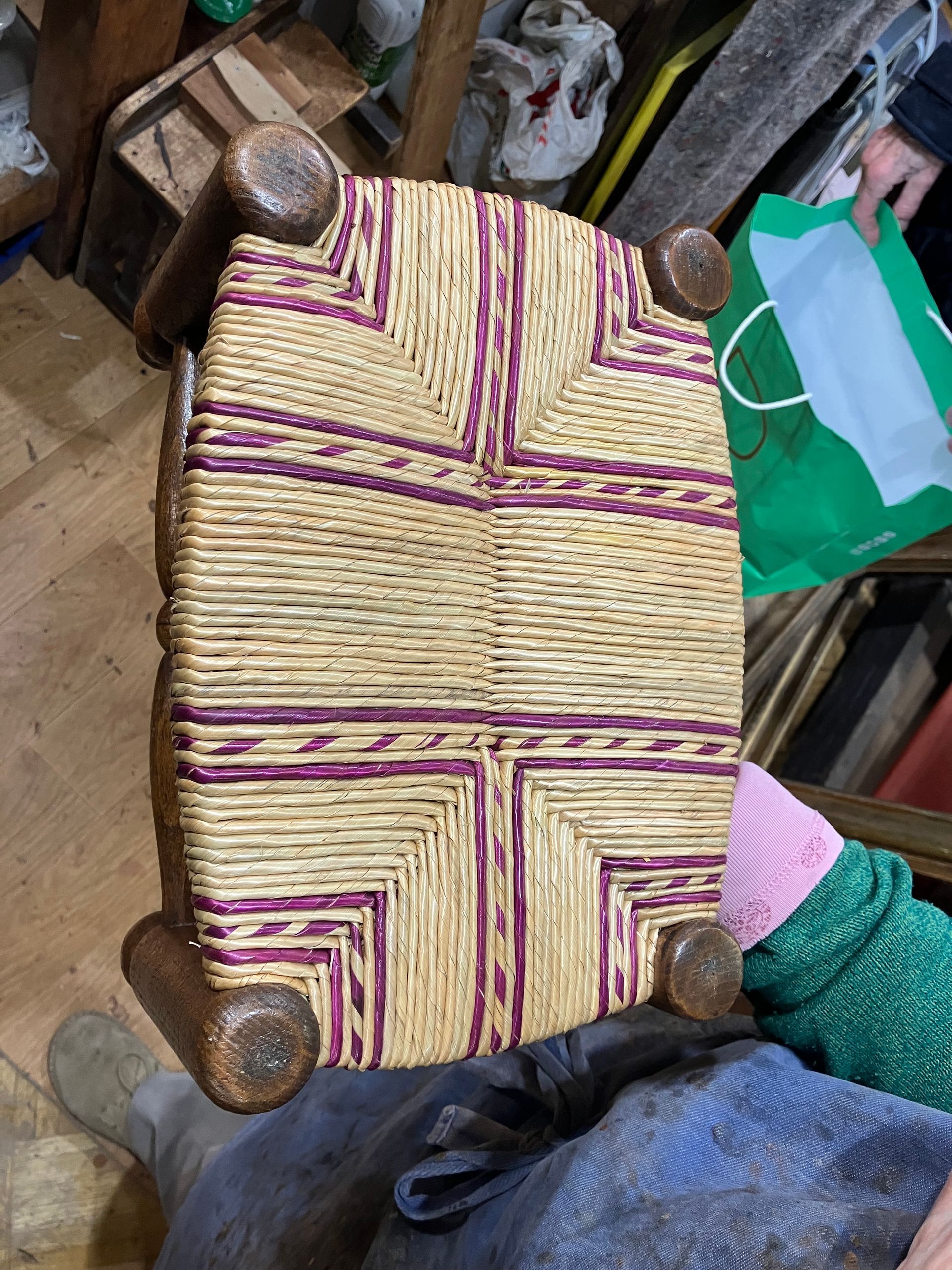 Natte en paille tressée bordée de violet, sur un cadre en bois, parmi du matériel d’atelier.