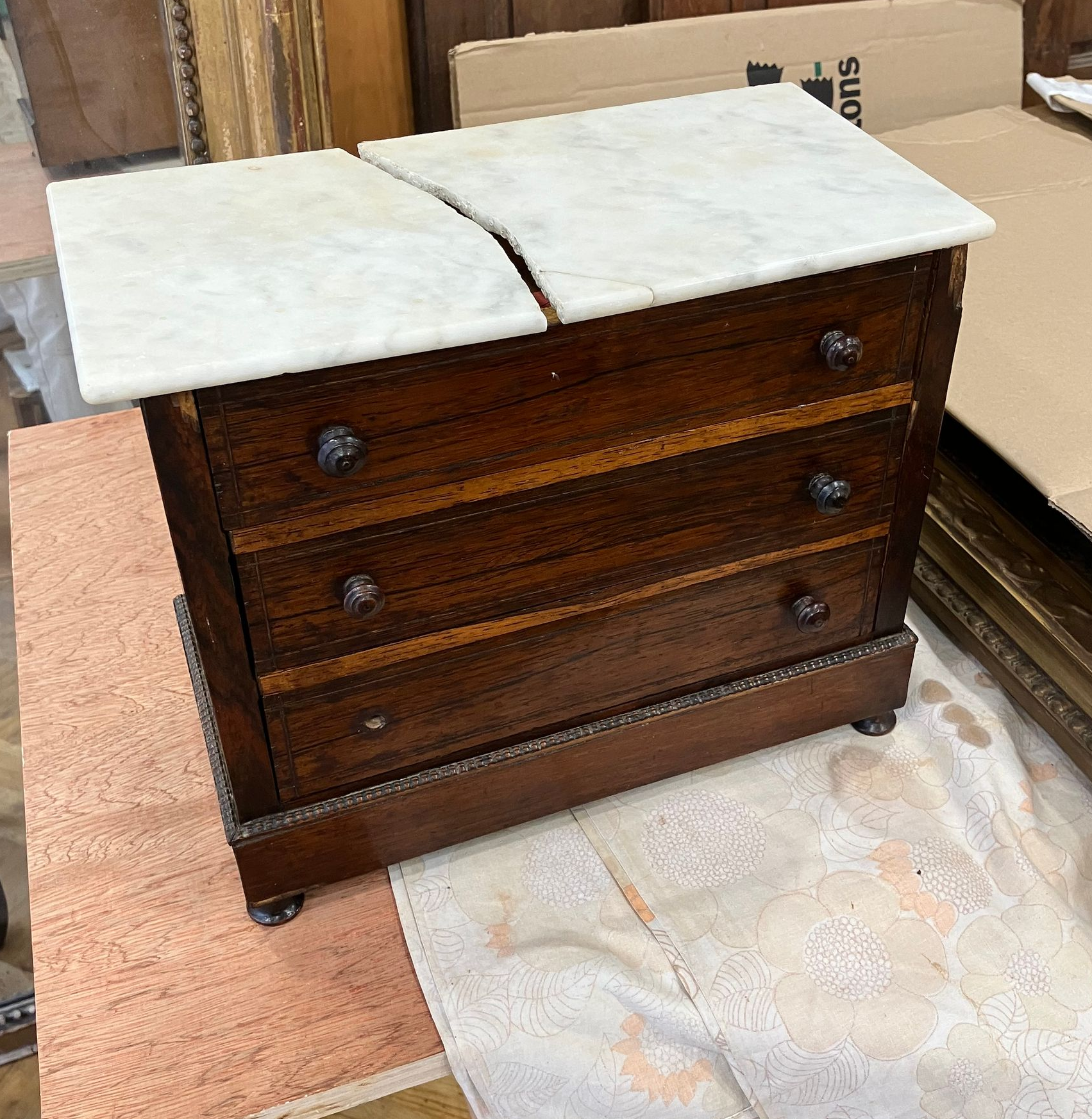 Petite commode en bois foncé à trois tiroirs, avec un plateau en marbre blanc brisé, dans un décor de type entrepôt