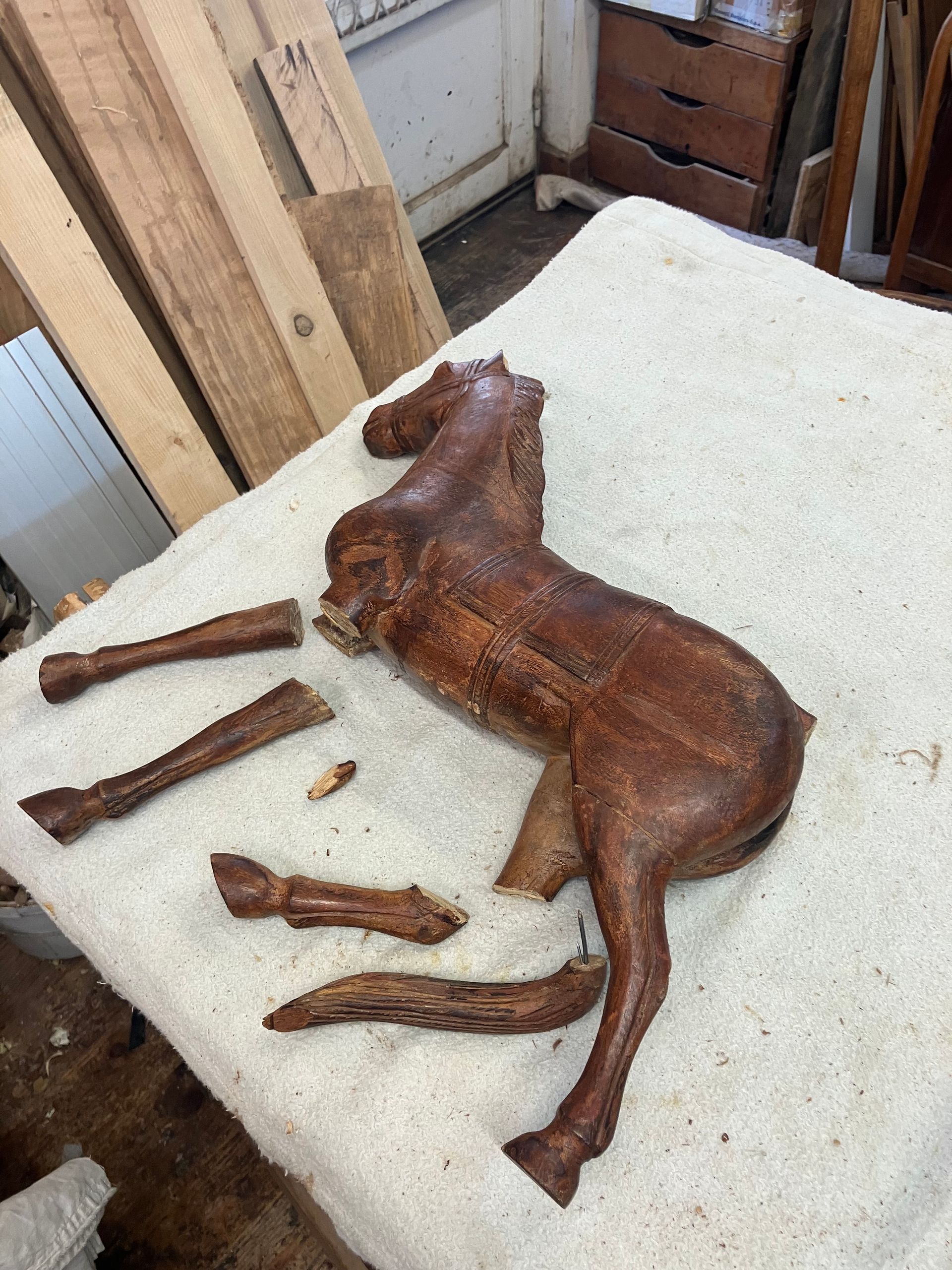 Figurine en bois marron sculptée en forme de cheval, avec les pattes détachées, posée sur une surface blanche dans un atelier