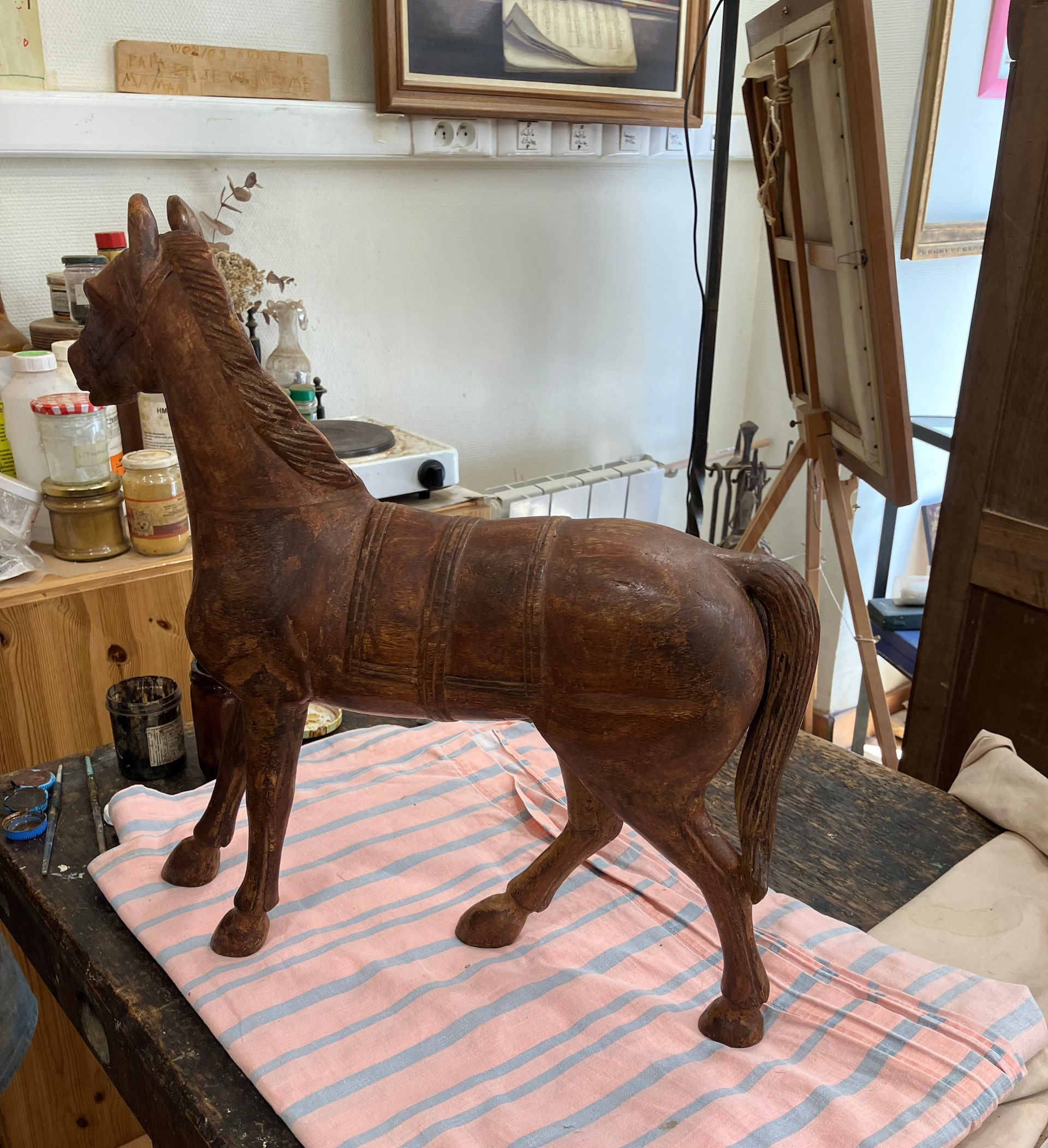 Sculpture de cheval brune posée sur un tissu rayé dans un atelier